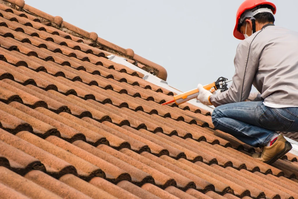 A roofer applying sealant to a terracotta roof during a Tile Roof Replacement